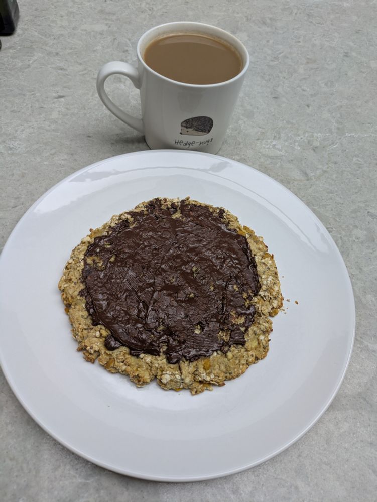 A giant cookie with chocolate on the top with a cup of coffee.