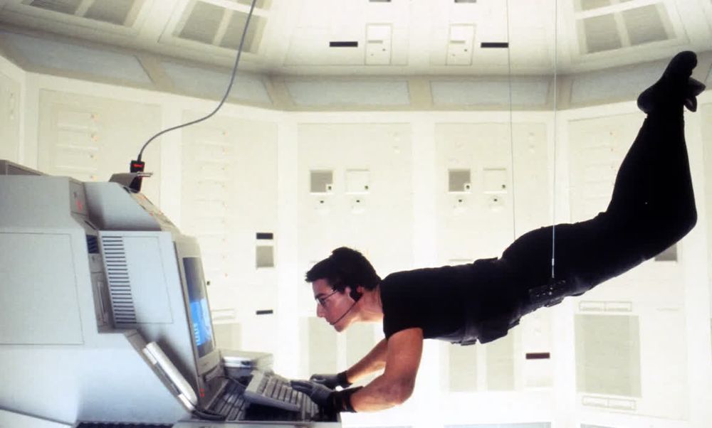 A picture of Tom Cruise as Ethan Hunt from Mission Impossible, typing on a computer while suspended by cables.