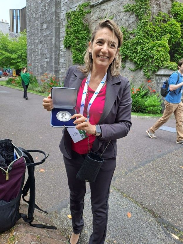 Photo of Licia Verde, chair of arXiv Science Advisory Council, smiling and holding the Jocelyn Bell Burnell Inspiration Medal awarded to arXiv in 2025.