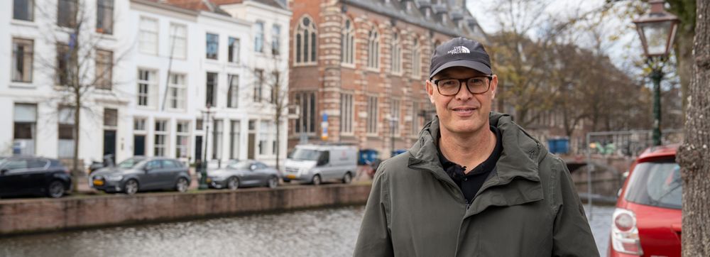Ruurd Kok met bril en een petje op voor de gracht voor het Academiegebouw in Leiden.