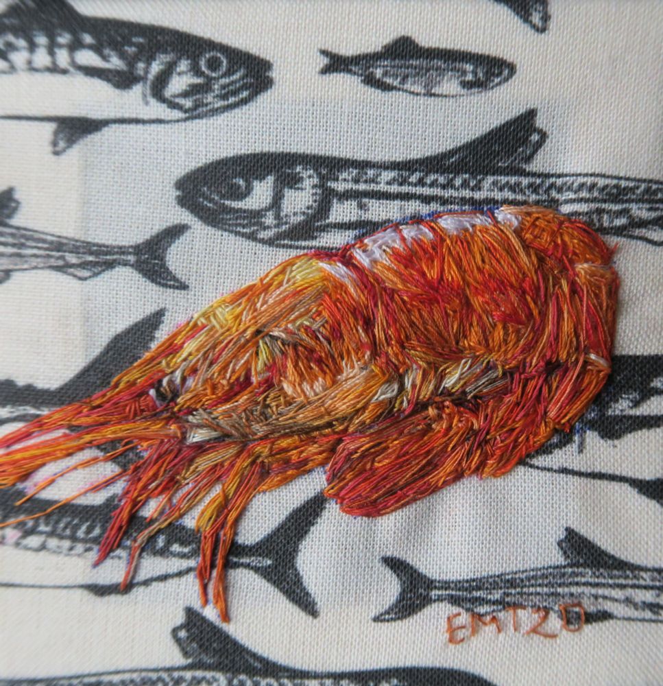 Hand embroidered orange/ red coloured cooked shrimp on a black and cream  fish pattern fabric background 