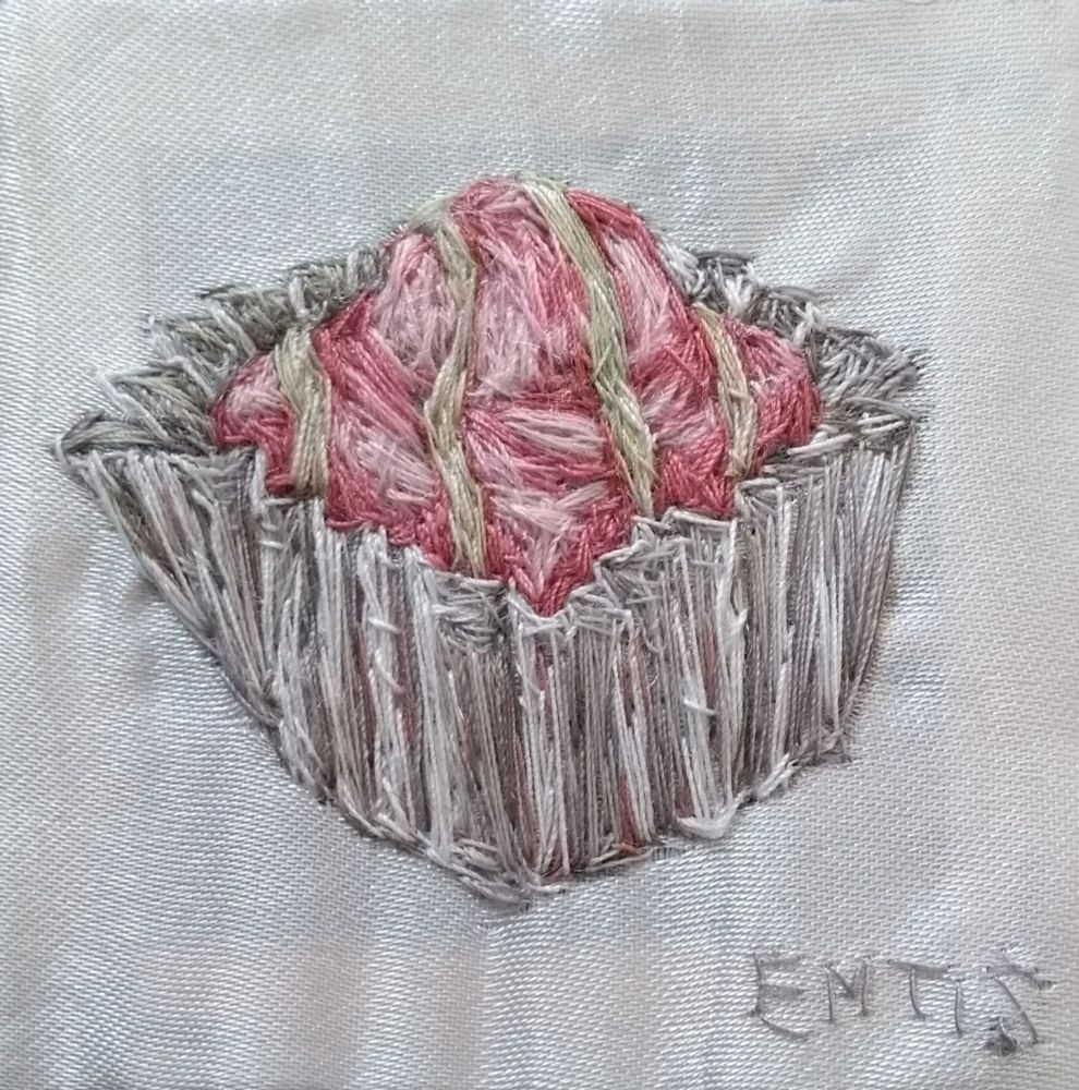 Hand embroidered pink French Fancy cake in case on a white satin background 