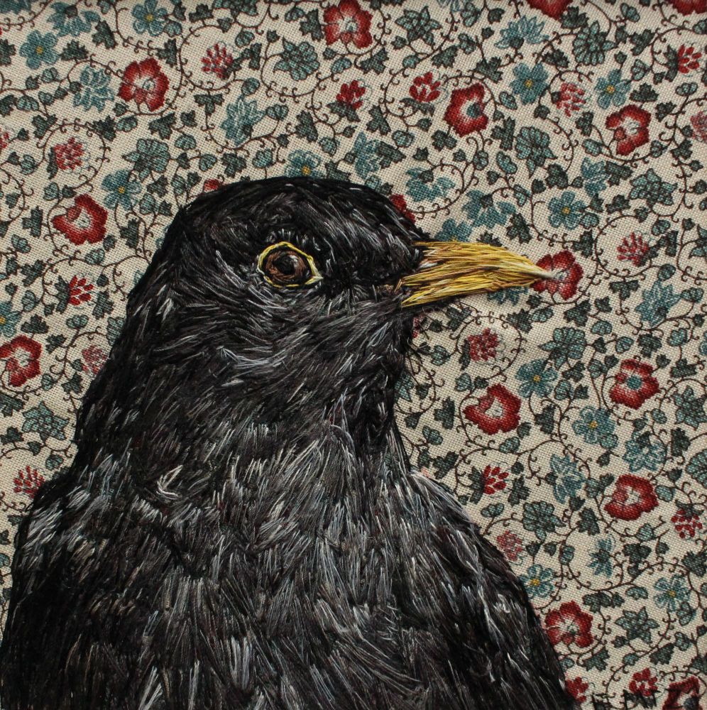 A hand embroidered male blackbird head to mid chest on an autumnal floral and vine patterned fabric background