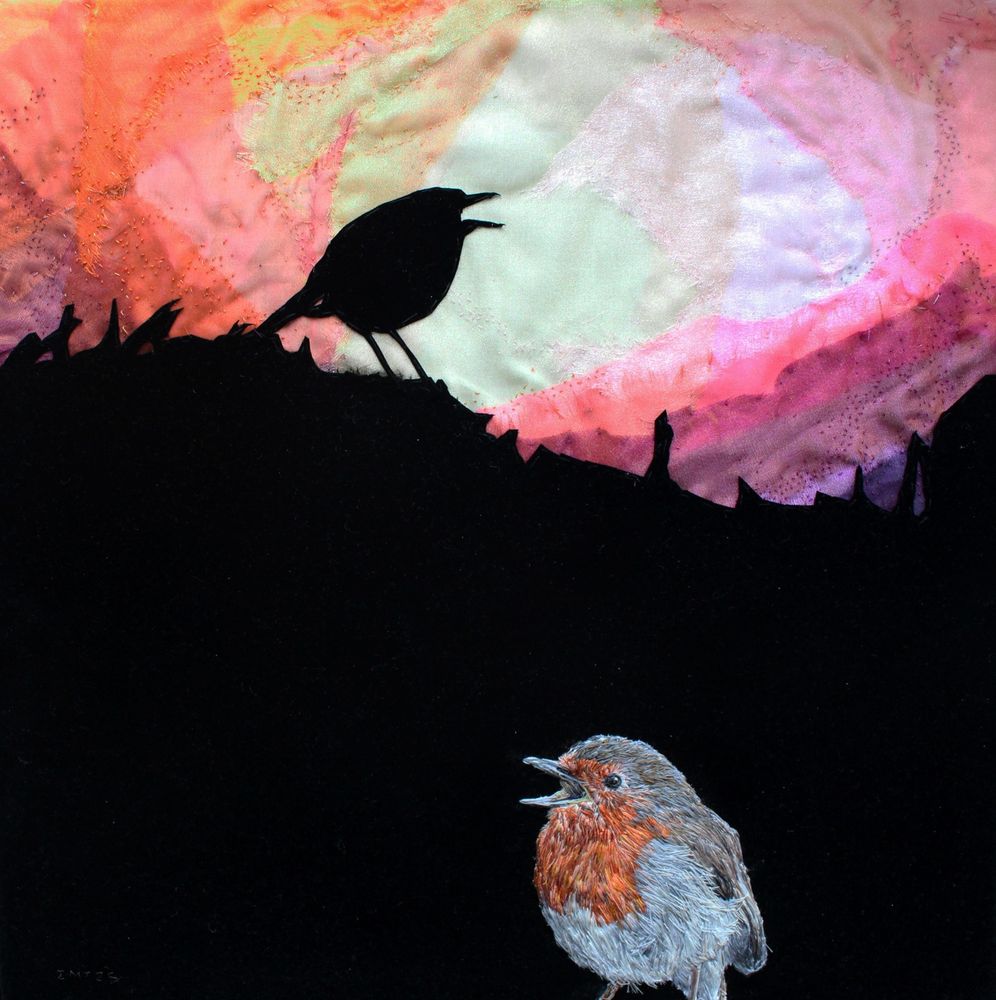 A hand embroidered singing Robin in the foreground on a black fabric silhouette of a Robin singing on a sunrise/sunset colours of layered organza