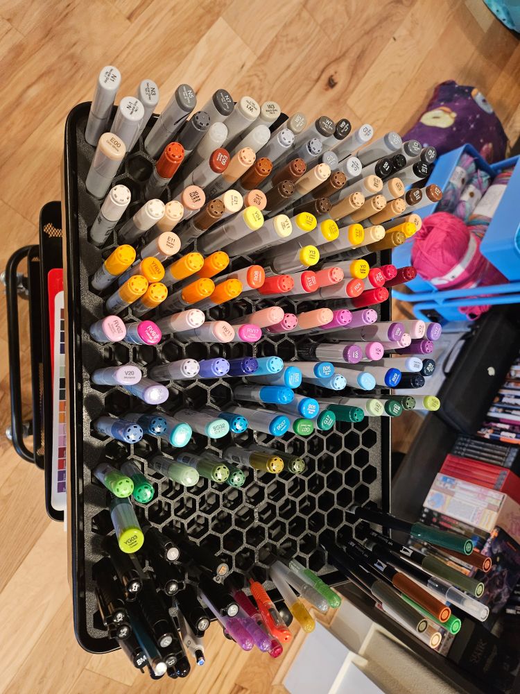 A picture of the top layer of 3 teir cart, which has a 3d printed honeycomb patterned tray that is holding copic markers. 