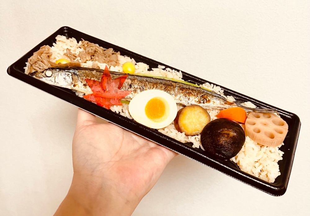 焼き秋刀魚(まるまる1尾)、茹で卵、さつまいも、椎茸、蓮根、人参、舞茸、銀杏がのった炊き込みご飯のお弁当。