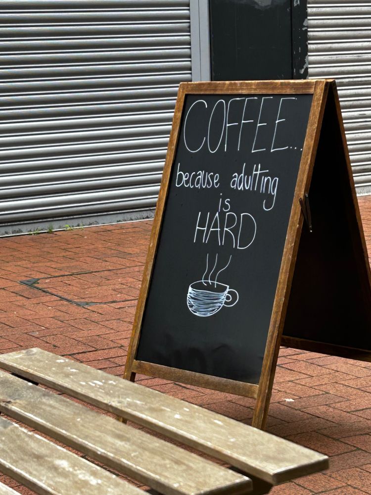 A-board at a coffee shop. Text: “Coffee because adulting is hard.”