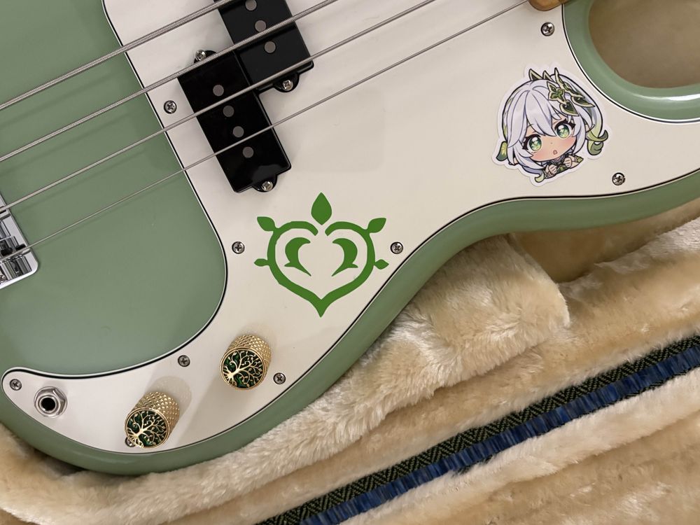 A close up of the decals I placed on my Fender bass, including custom knobs, a sticker of Nahida, and a dendro symbol from Genshin Impact.