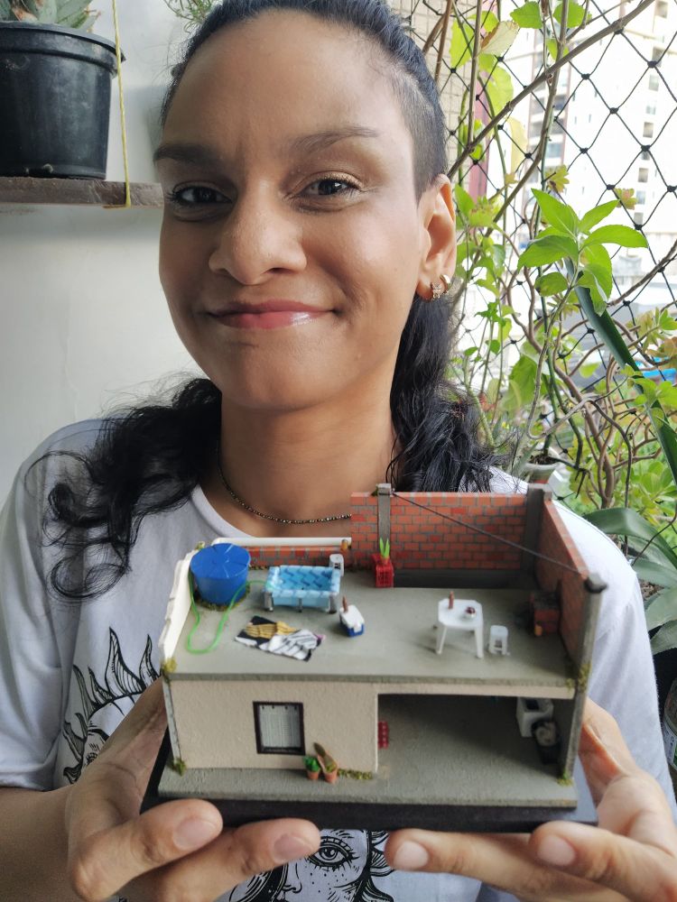 Eu uma mulher adulta de cabelo preto longo de camiseta branca segurando uma miniatura de casinha com laje 