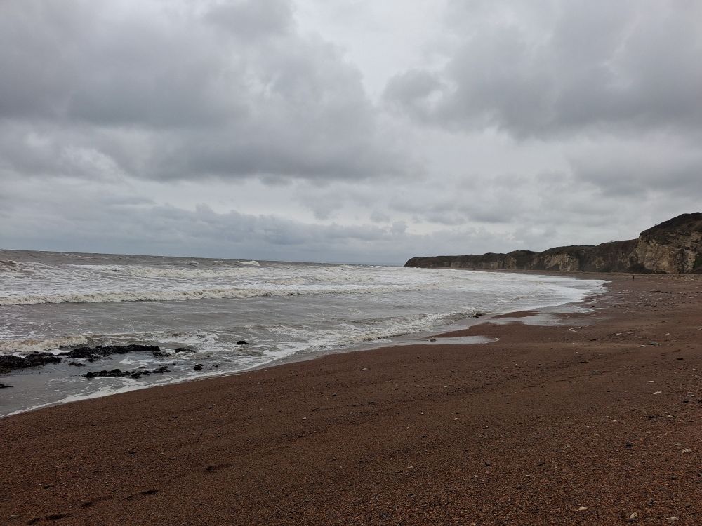 A large beach with grey sea and sky. There is nobody on the beach. 