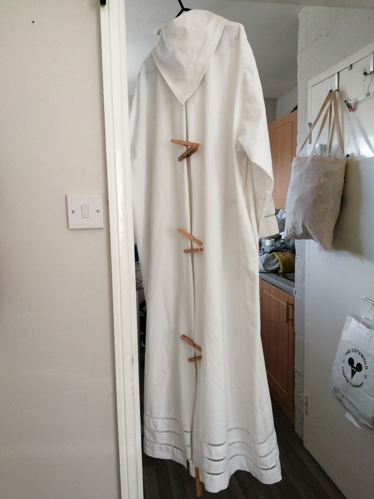 The back of an alb (a long white robe) hanging up with pegs on the pleats to keep them in place. 