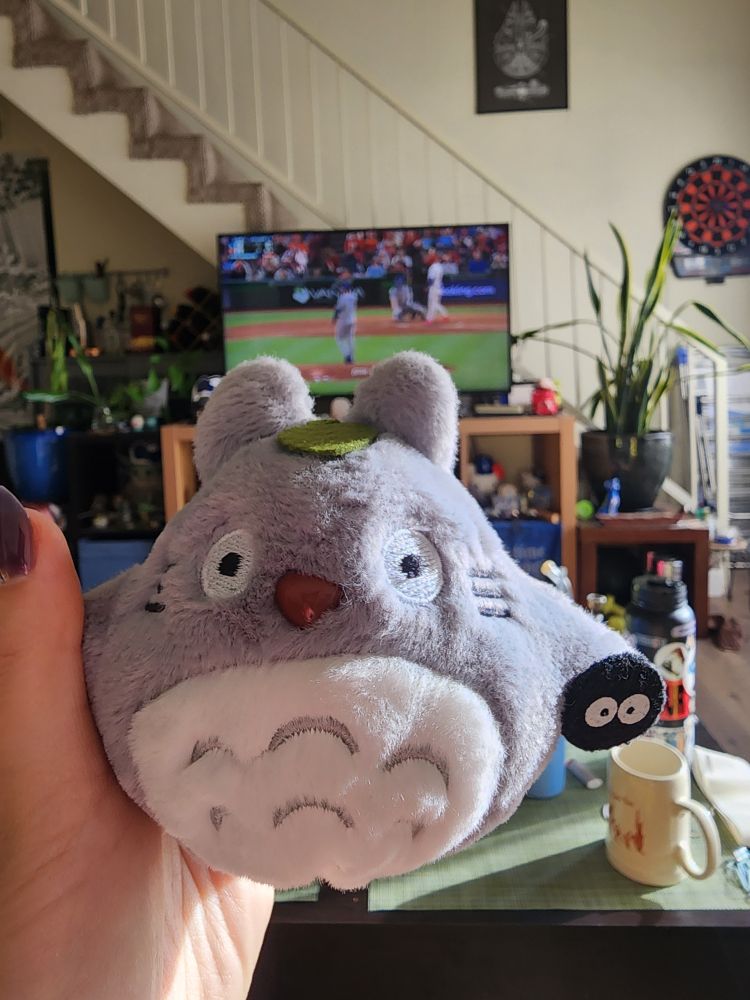 Small stuffed totoro doll with TV on in the background