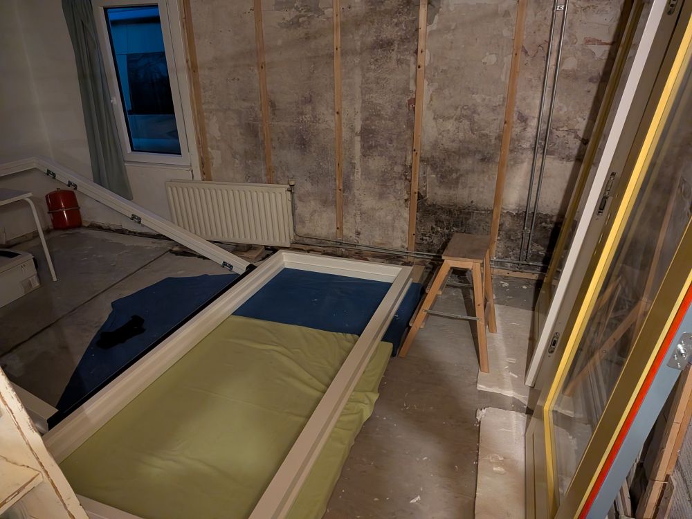 In een kale kamer liggen twee grote witte kozijnen, rechts staan twee tuindeuren die okergeel zijn geverfd.