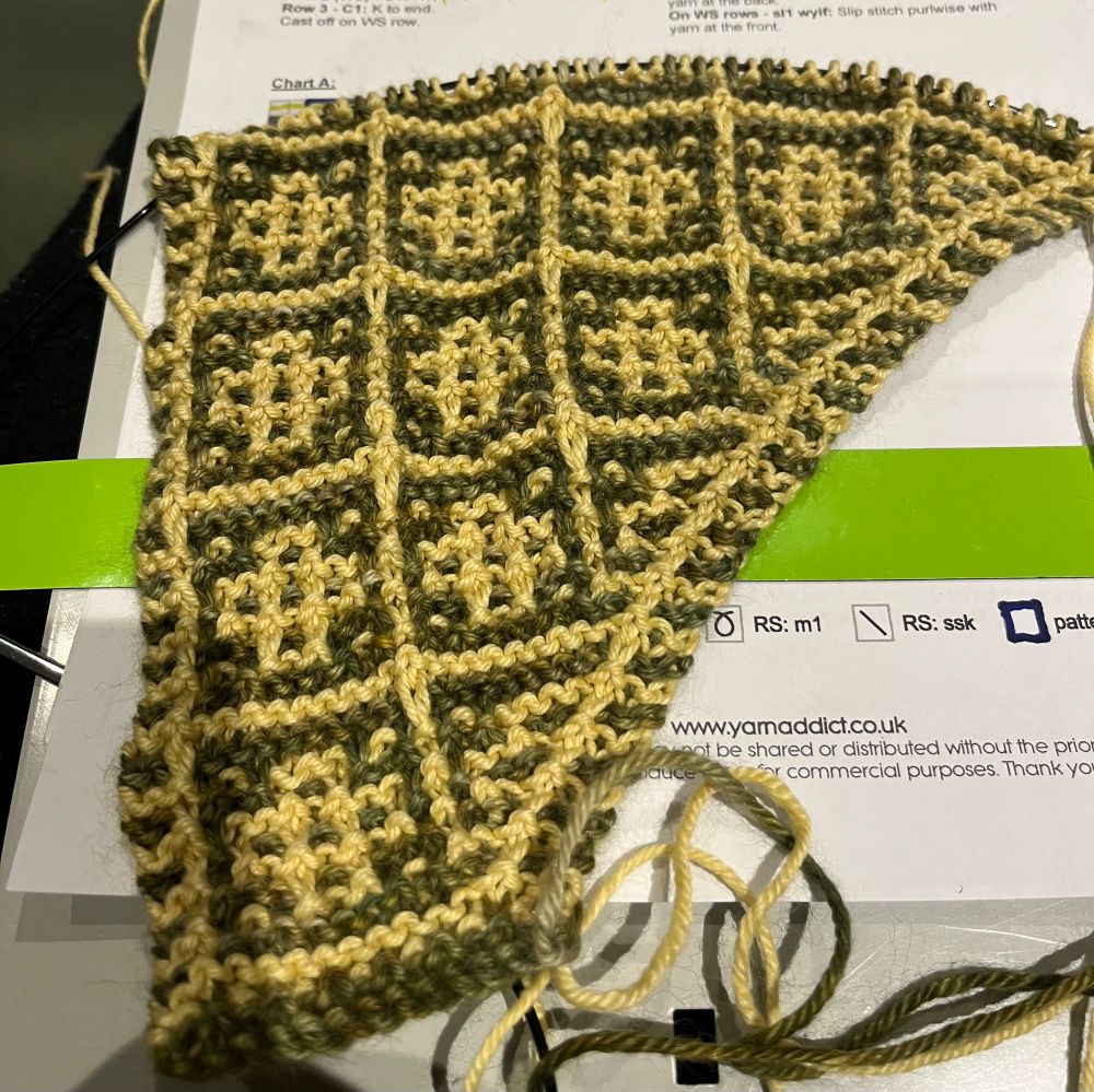 Half finished scarf knitted in green and yellow mosaic