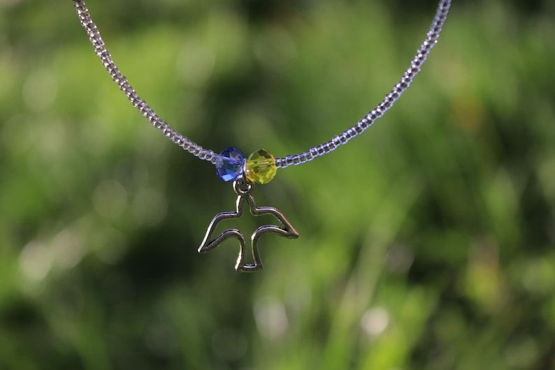 Collier en perles de verre dont une perle bleue et une jaune avec en pendentif une colombe de paix en métal.
