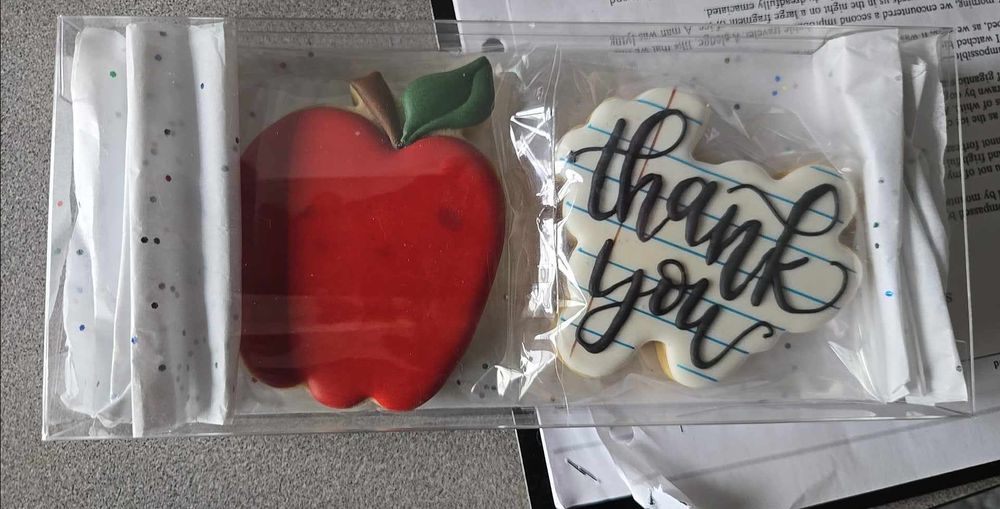 Two large sugar cookies, one in the shape of a red apple, and one saying "Thank you" 