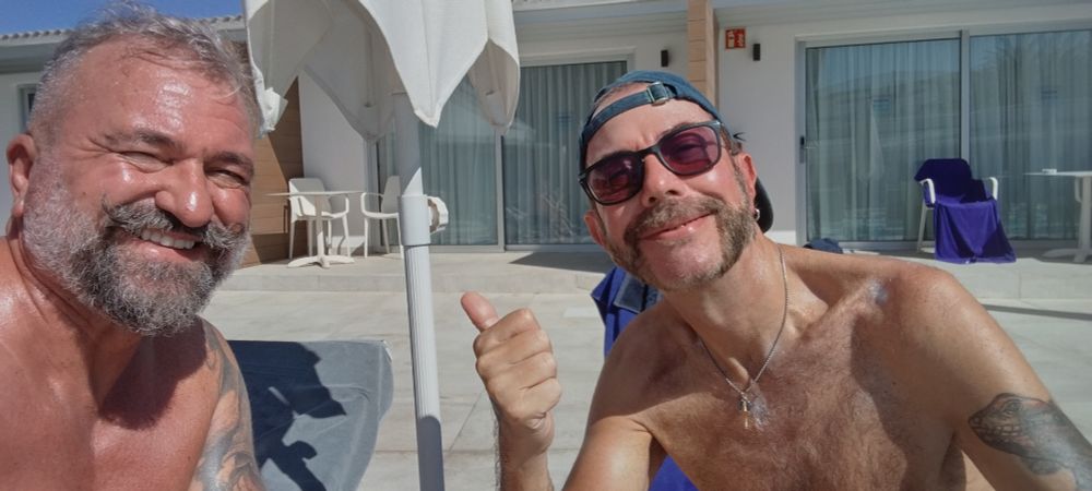 Two shirtless gay men on sunloungers