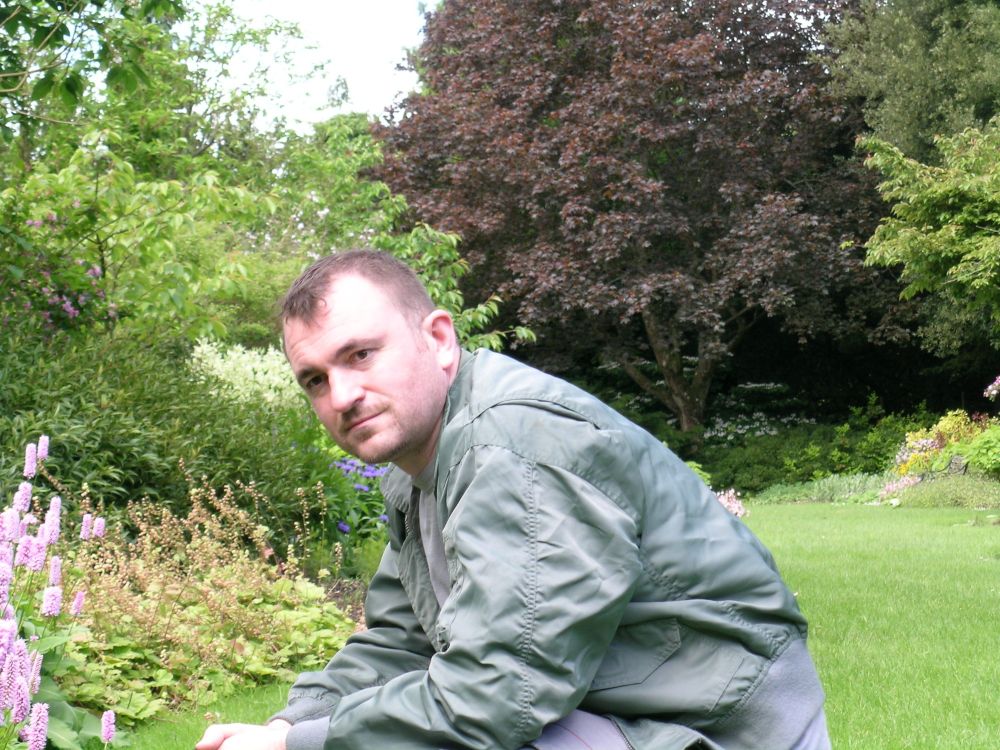 A man in his 30s crouches in a garden