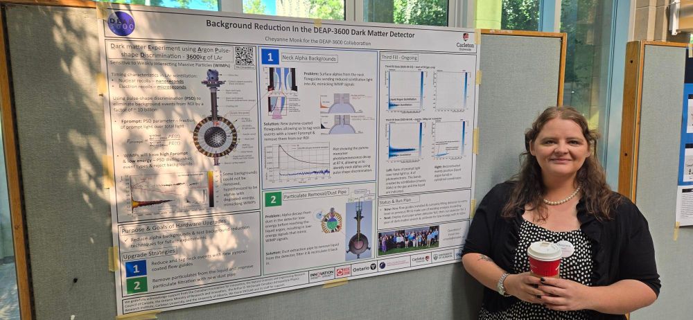 A person standing next to a scientific poster titled “Background Reduction in the DEAP-3600 Dark Matter Detector.” The poster includes diagrams, graphs, and descriptions of experimental methods. The person is holding a coffee cup and smiling at the camera.