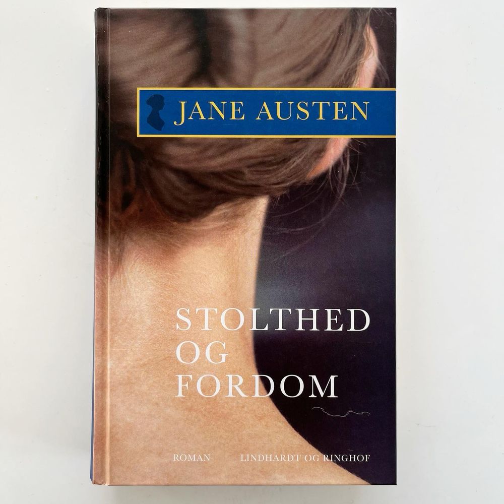 The Danish translation of Pride and prejudice on a white table. The cover shows the neck of a person with long hair with their hair up.