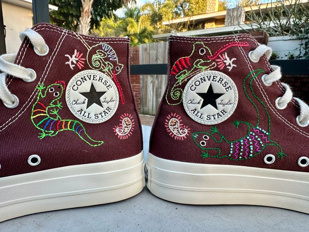 The other side 

A pair of brown hightop converse sneakers either colorful lizards embroidered on the sides as well as pink and yellow paisleys along the soles 
