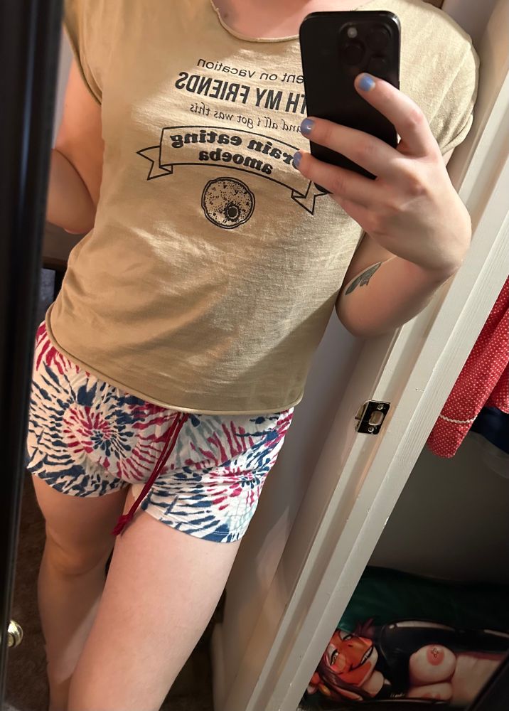mirror selfie showing tie dye shorts and a shirt that says brain eating amoeba