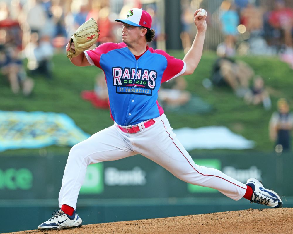 LHP Shea Sprague pitches at Fluor Field in the Ranas de Rio uniform (white pants, blue jersey with very pink sleeves, blue/white/pink cap) of the Greenville Drive.