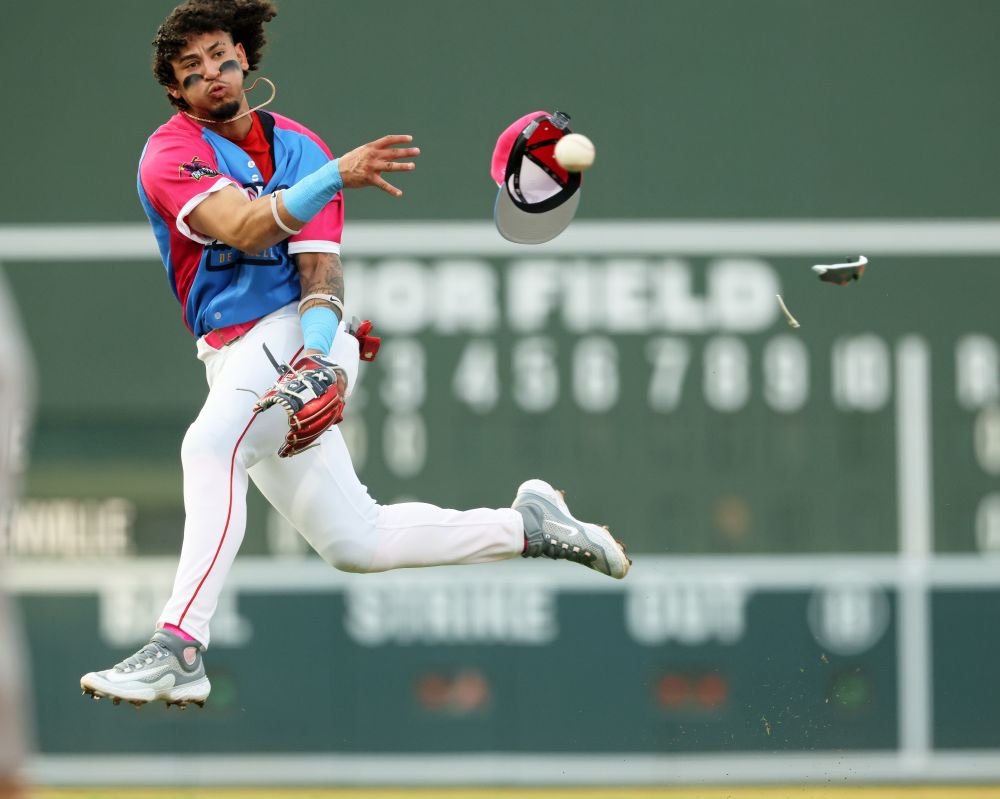 Infielder Fraymi De Leon goes airborne after his throw at Fluor Field in the Ranas de Rio uniform (white pants, blue jersey with very pink sleeves, blue/white/pink cap) of the Greenville Drive. Flying away from him is the ball... and his cap, and pieces of his sunglasses, which got in the way of his throw.