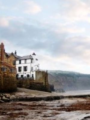  A deserted beach with cliffs in the background and some old, tall houses in the foreground. The nearest house is white and I think it's Georgian. There are some barrels on the beach that suggest smugglers have left casks of rum.
