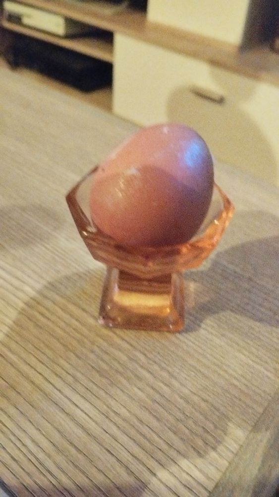 Ein braunes Ei in einem rötlichen, alten Likörgläschen, es liegt schief.