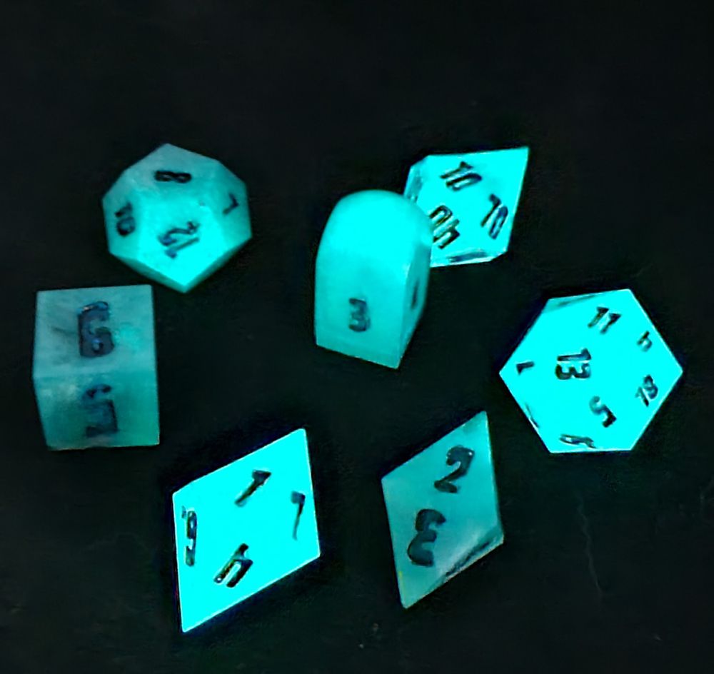 The same set of blue-green dice in the dark after being exposed to UV light. The set glows a bright blue-green, very similar to what they look like in the daylight. 