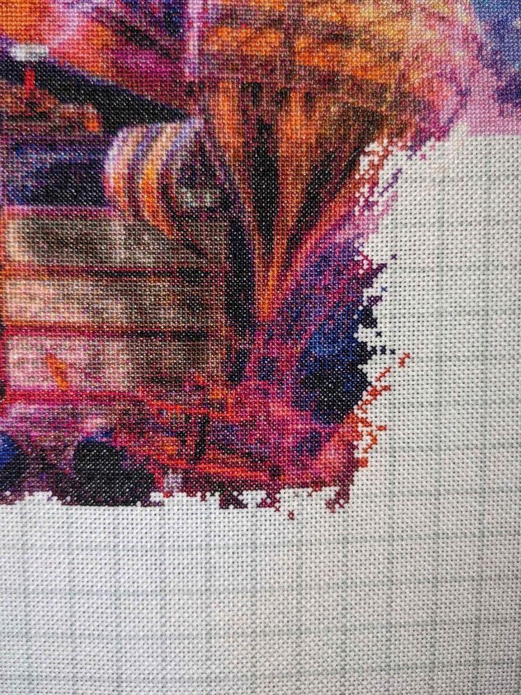 Close of up a portion of a cross stitch piece showing a stack of books with a steam-punk-esque hot air balloon flying in front of them.
