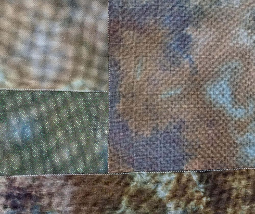 A selection of "Bogwood" fabric on Aida, Opalescent Aida, Lugana, and Linen - each giving a slightly different variation of deep blues, browns, and purple colors.