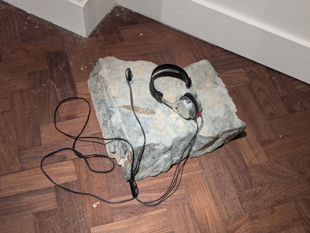 Pic of a large stone on the ground with headphones connected to it 