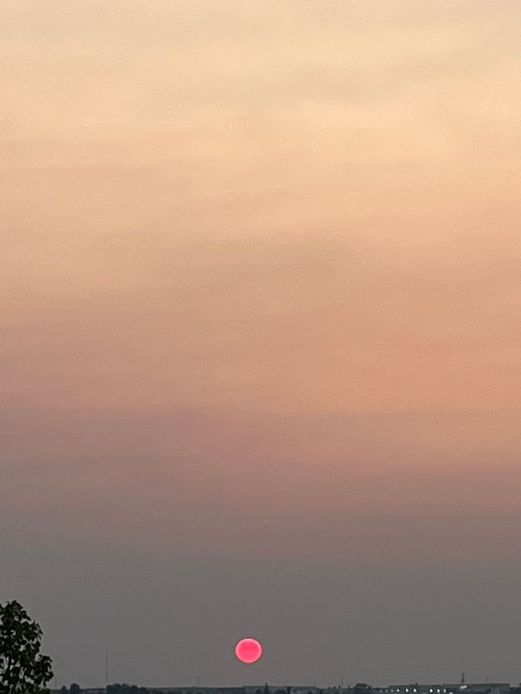 Puesta de sol con un cielo gris difuminado y naranja suave en la parte superior. Y un sol circular y rojo en la parte inferior 
