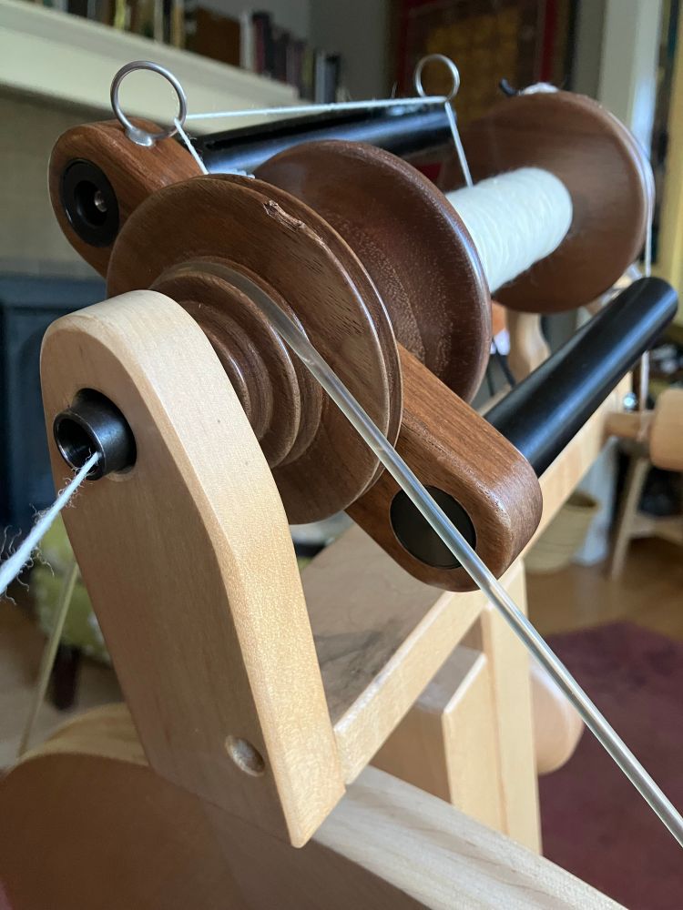 A close view of the mother-of-all and flyer on a Lendrum upright spinning wheel. The front maiden (the upright in the foreground) had been coming loose from the Mother Of All (the horizontal part) and tilting forward. This was mechanically awkward for the rotation of the flyer. Glued, clamped, rested, and all better now. 