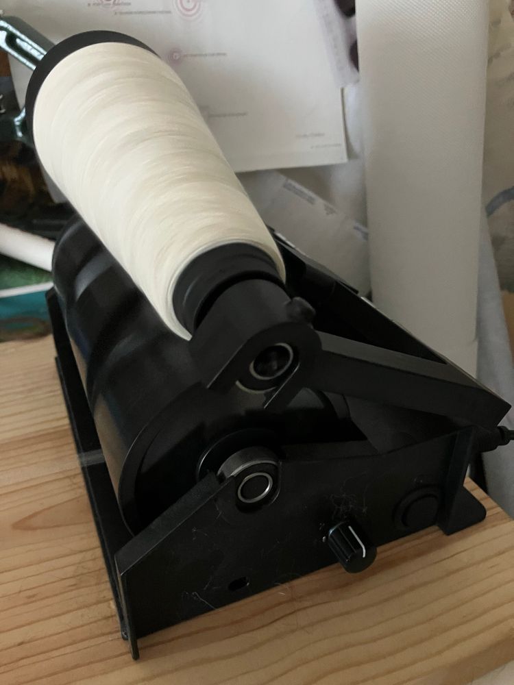 A Dreaming Robots electric cone winder on a wooden board. The machine is operating, winding white wool onto a black plastic cone. 