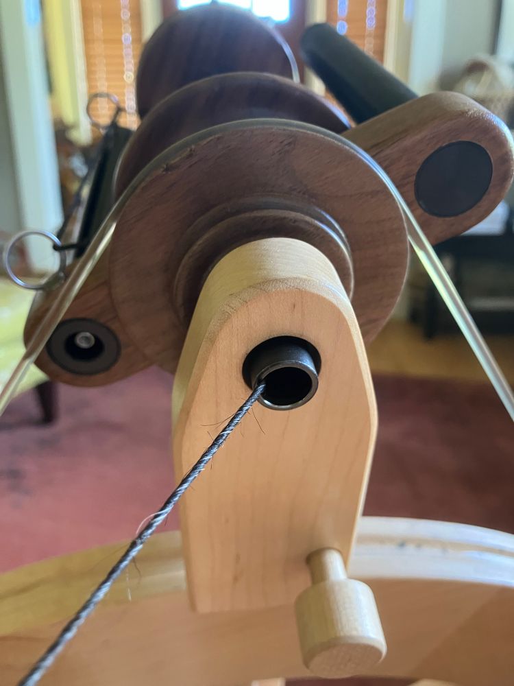 A close view of black and gray double coated wool yarn forming at the orifice of a spinning wheel. 