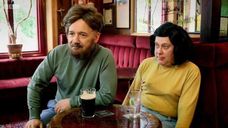 Vic and Bob as Mulligan and O'Hare in a pub. A pint of Guinness is on the table. Vic is wearing a mustard coloured top and his bosoms are sagging.