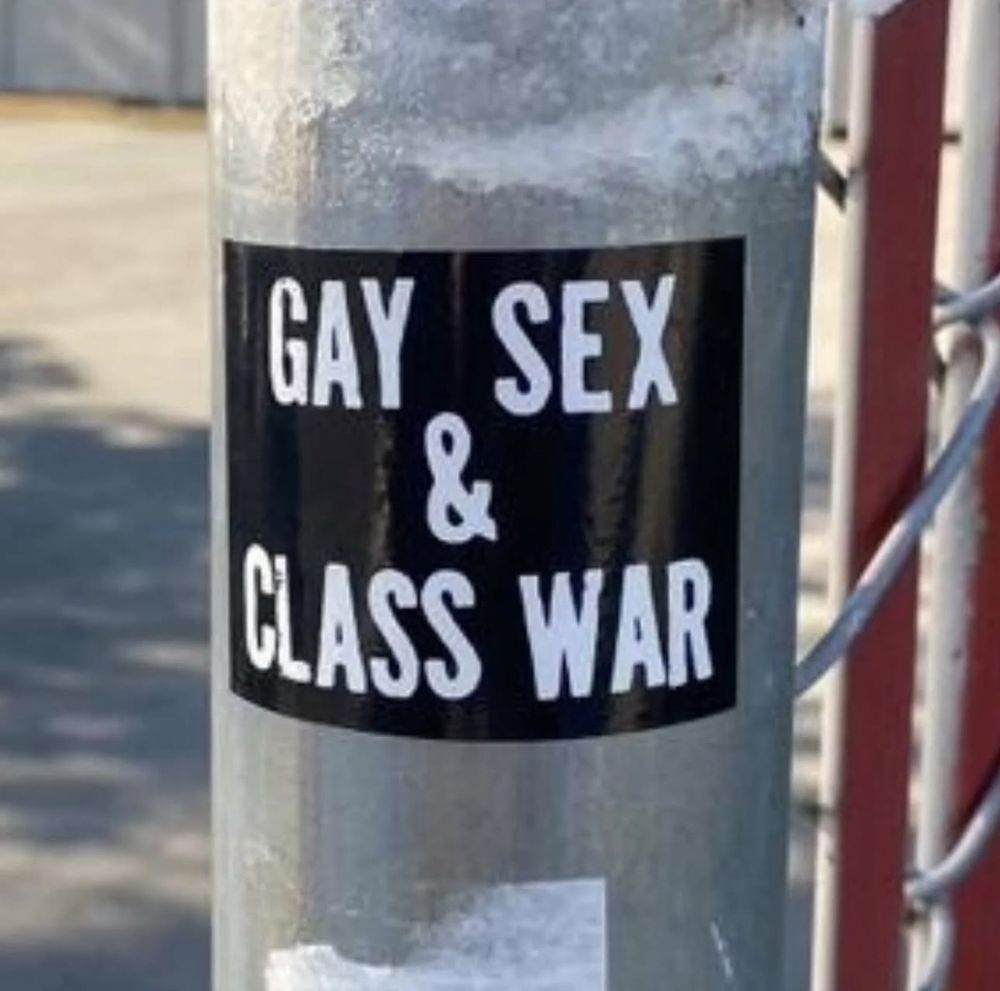 A metal pole has a black sticker on it that says “gay sex and class war”.