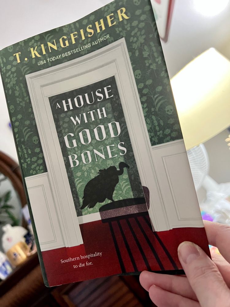 Photo of myself holding book cover for “house with good bones “by T Kingfisher.