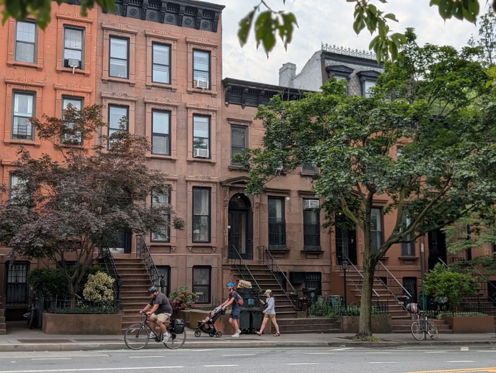 image of people with a stroller and someone riding their bike in front of brownstones