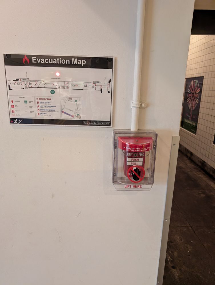 photo of the same fire alarm, with the sign now gone. the wall where the sign used to be is a slightly different color. 