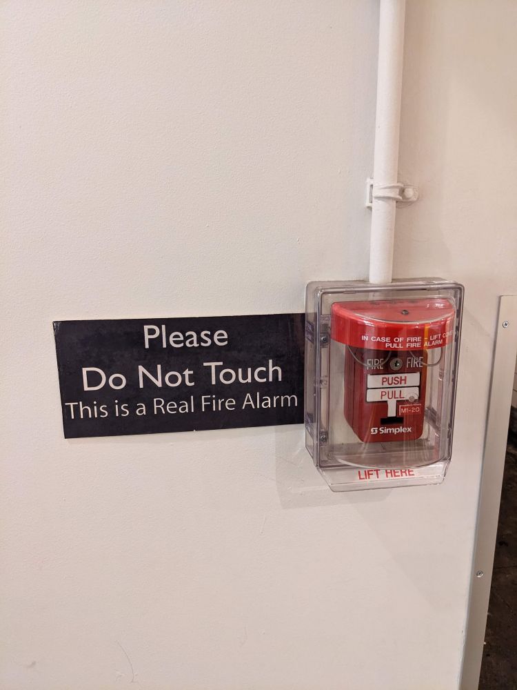 photo from January 2021, of a fire alarm with an accompanying sign that reads "please do not touch, this is a real fire alarm"
