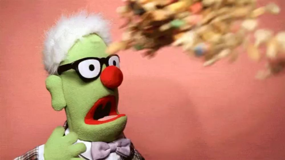 a green puppet with glasses and a red nose is blowing out cereal