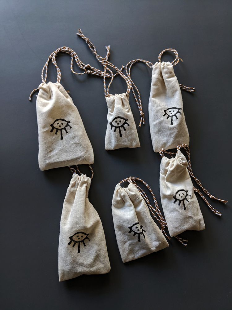 handmade drawstring sachet bag with block printed mysterious symbol on them resembling an eye with rays coming forth and three dots like iris' within