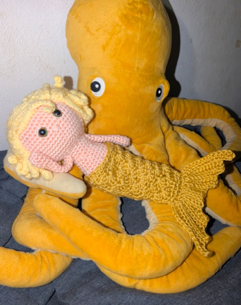 Stede doll, topless with a gold mermaid tail, lounging on a golden octopus