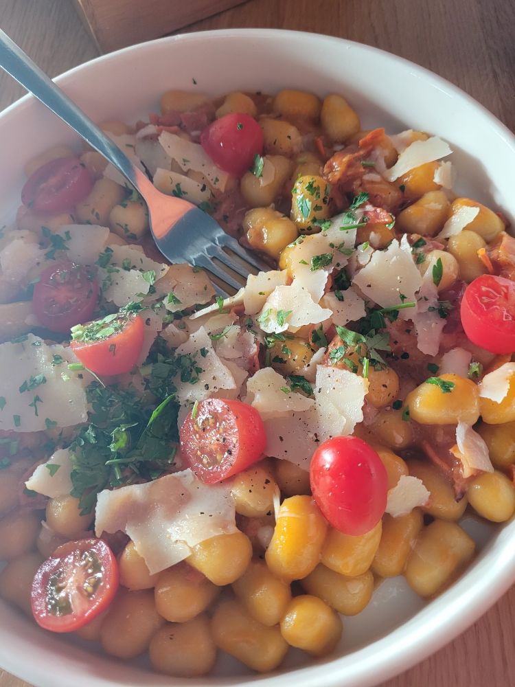 A plate of gnocchi in pumpkin sauce, with chorizo, grated parmesan and cherry tomatoes