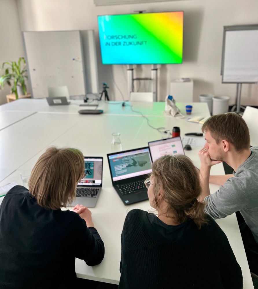 Das Wisskomm.de Team sitzt in einem Meetingraum, guckt auf die Seite und im Hintergrund sieht man eine Slide die „Forschung in der Zukunft“