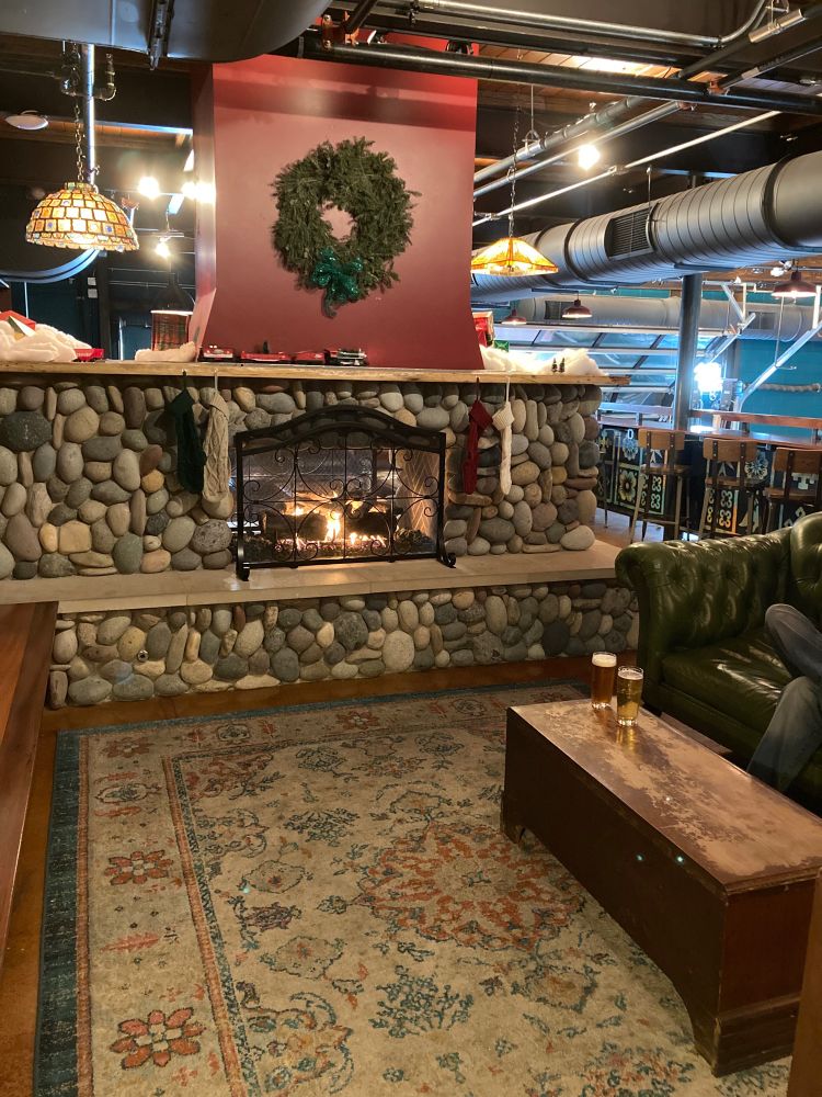 Upstairs at Lazarus Brewing, cozy stone fireplace and a couple beers on a coffee table on an old-looking rug. A Christmas model train runs along the mantle.